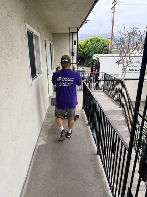 Twilight Movers crew member moving furniture through an apartment walkway with moving truck outside